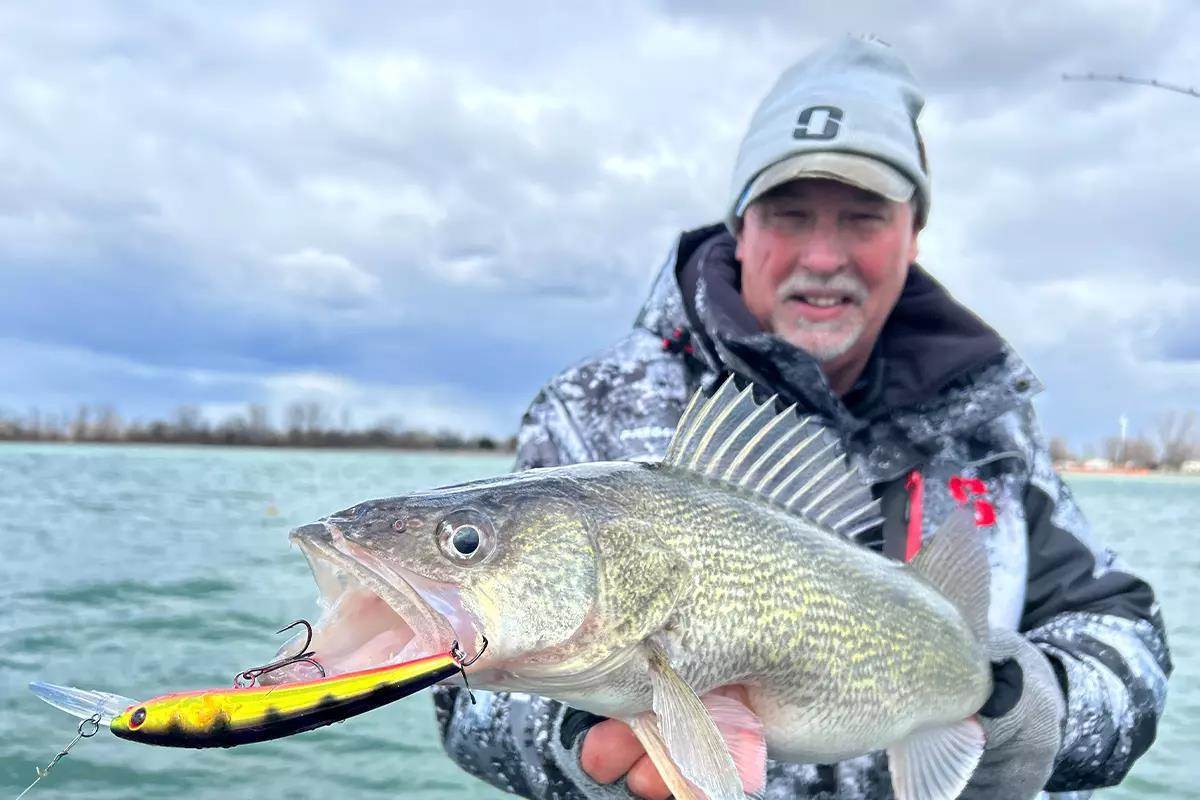 An angler holds up a caught walleye with a crankbait hanging from its lip. 