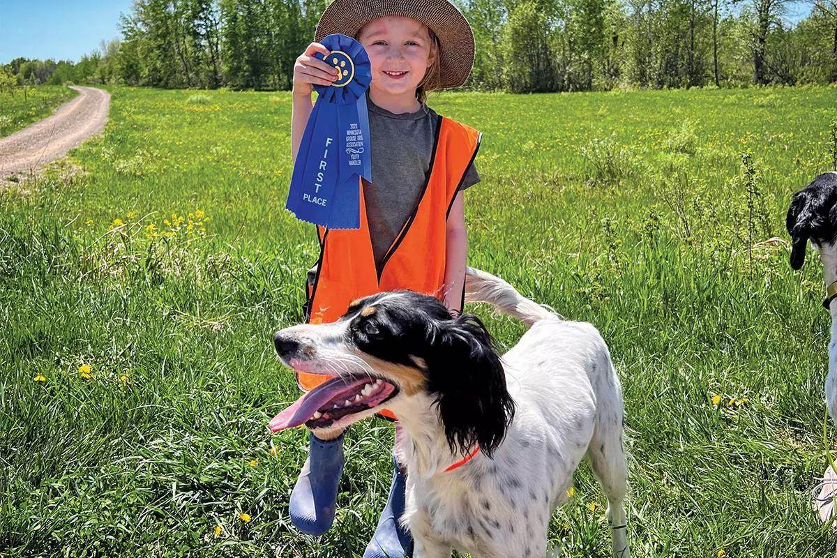 A young girl holds a ribbon next to a black and white English setter.