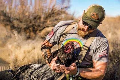 A hunter holds the head of a dog with porcupine quilt in its mouth.