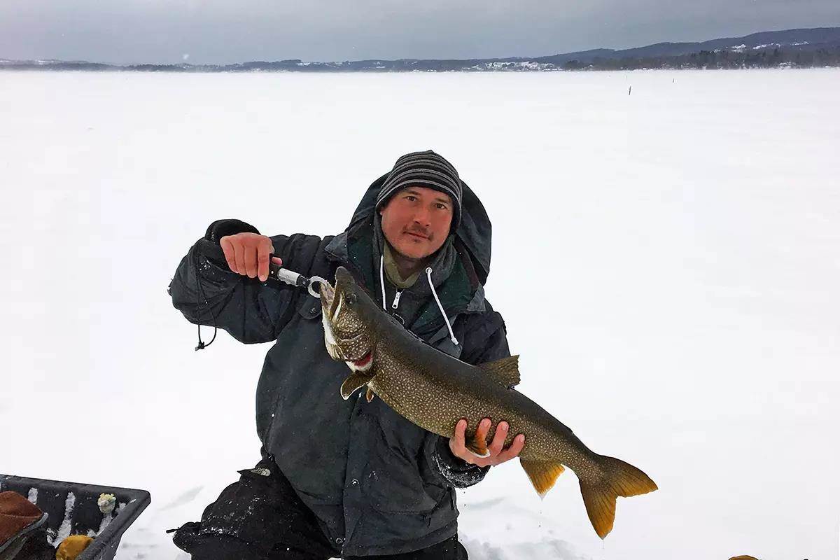 An ice angler holding a large lake trout for the camera. 