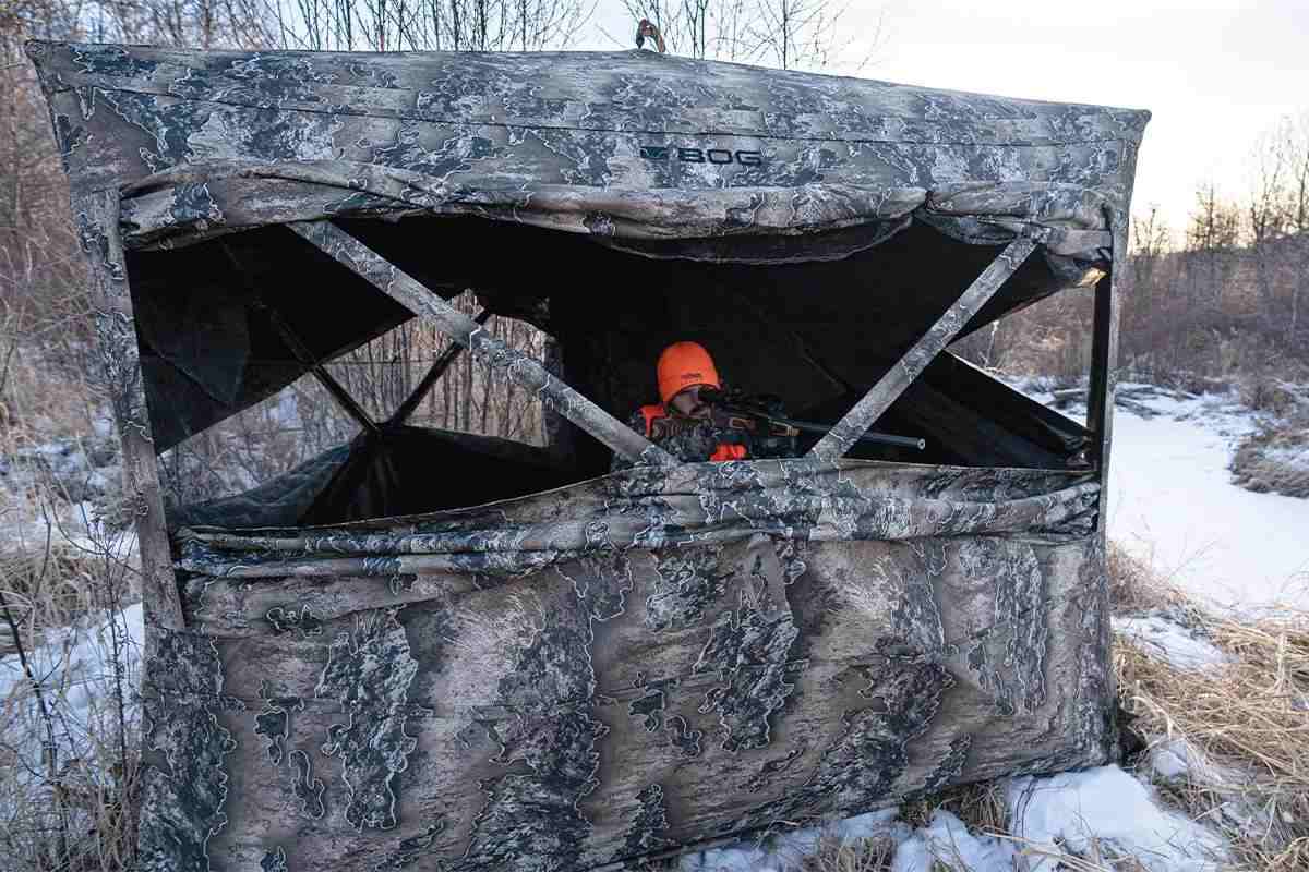 A hunter pokes his rifle out of a hunting blind during winter. 