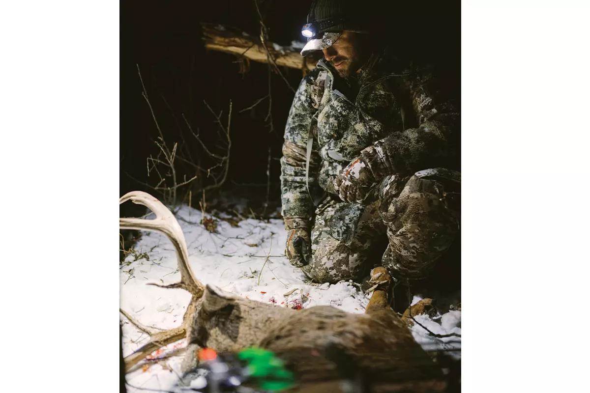 A hunter uses a headlamp to check out a downed white-tailed buck lying in the snow.