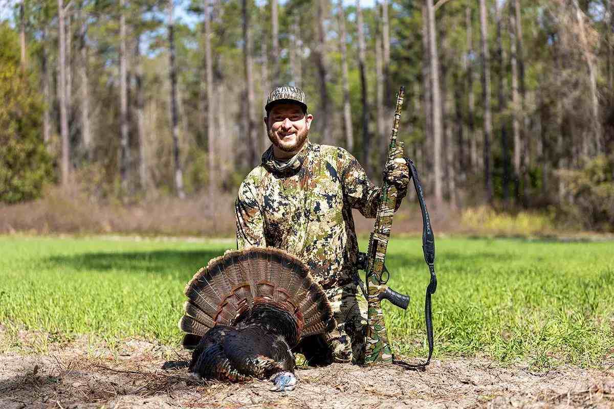 Turkey hunter posed behind harvested turkey with tail fan splayed out.