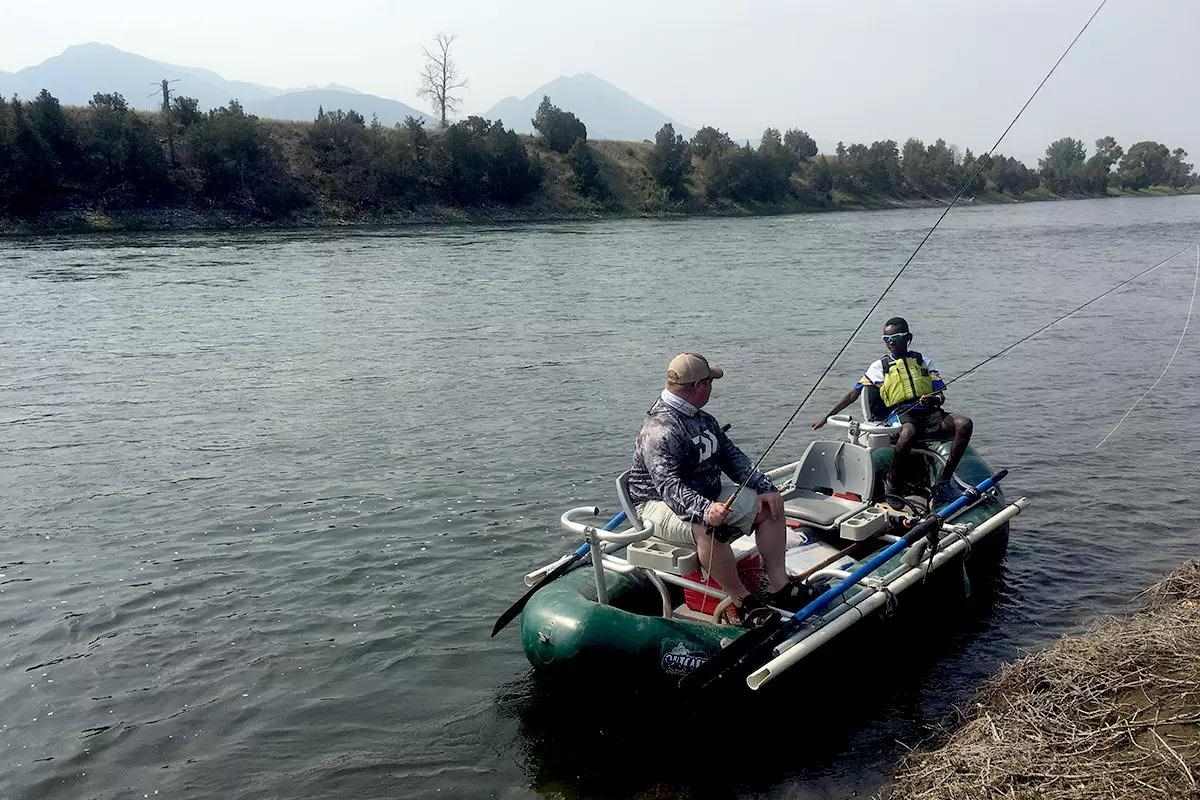 Two fly anglers in a green raft on a broad river; a child wearing a PFD and an adult not wearing a PFD.
