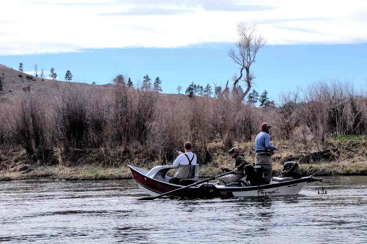 Three fly fisherman in a red and white drift boat floating downstream.