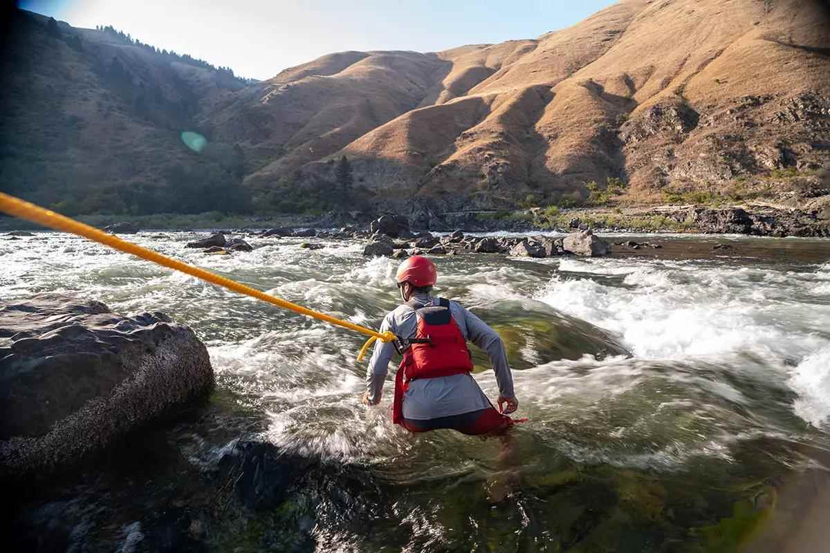 A river rescue professional wearing a helmet and PFD strapped to a rope in a fast-water section of a desert canyon river.