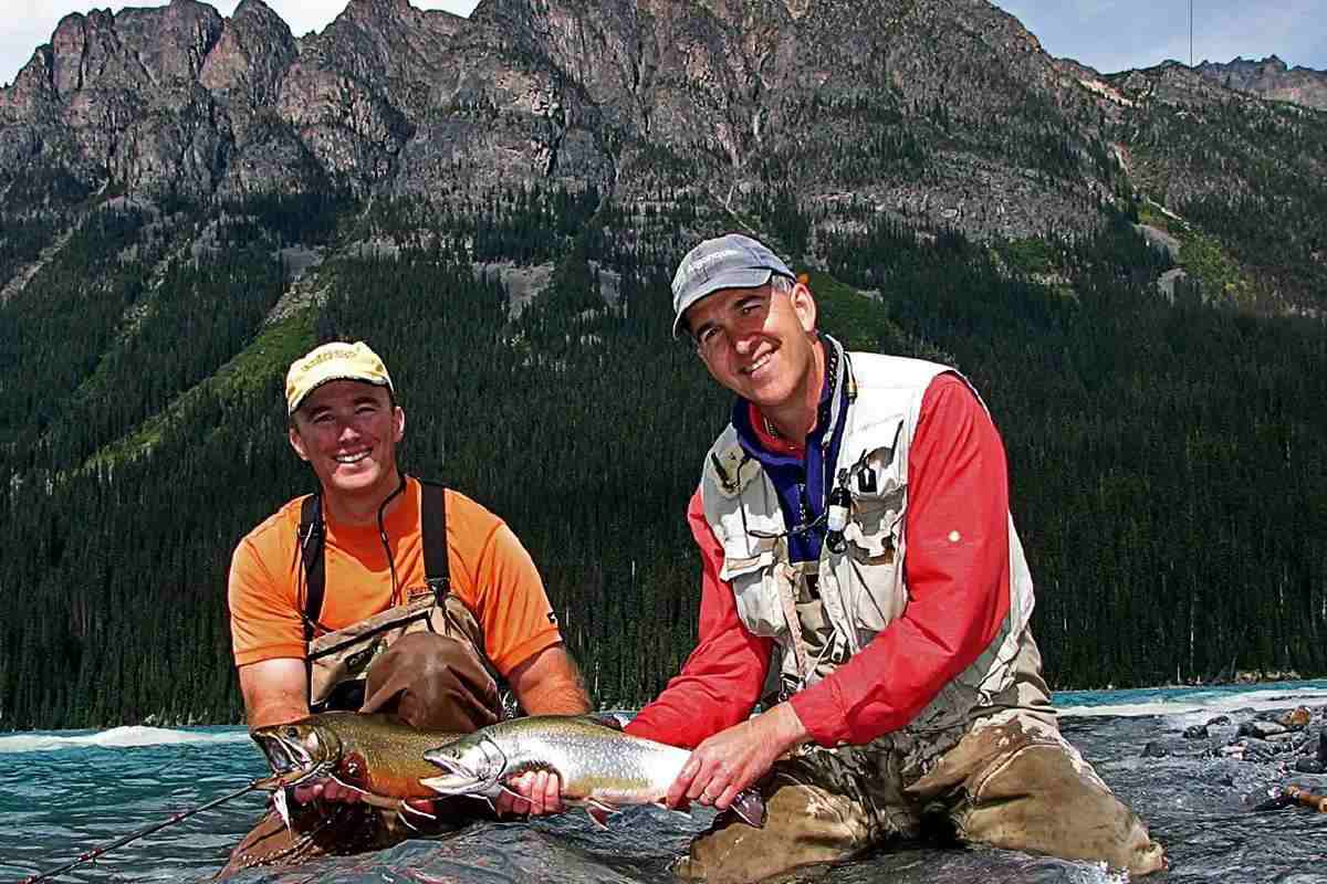 Two men kneeling in the shallows of a mountain lake, each holding a large brook trout.