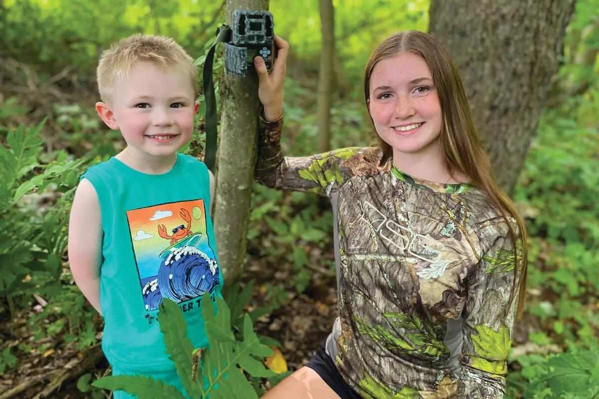 sister setting trail camera as younger brother looks on