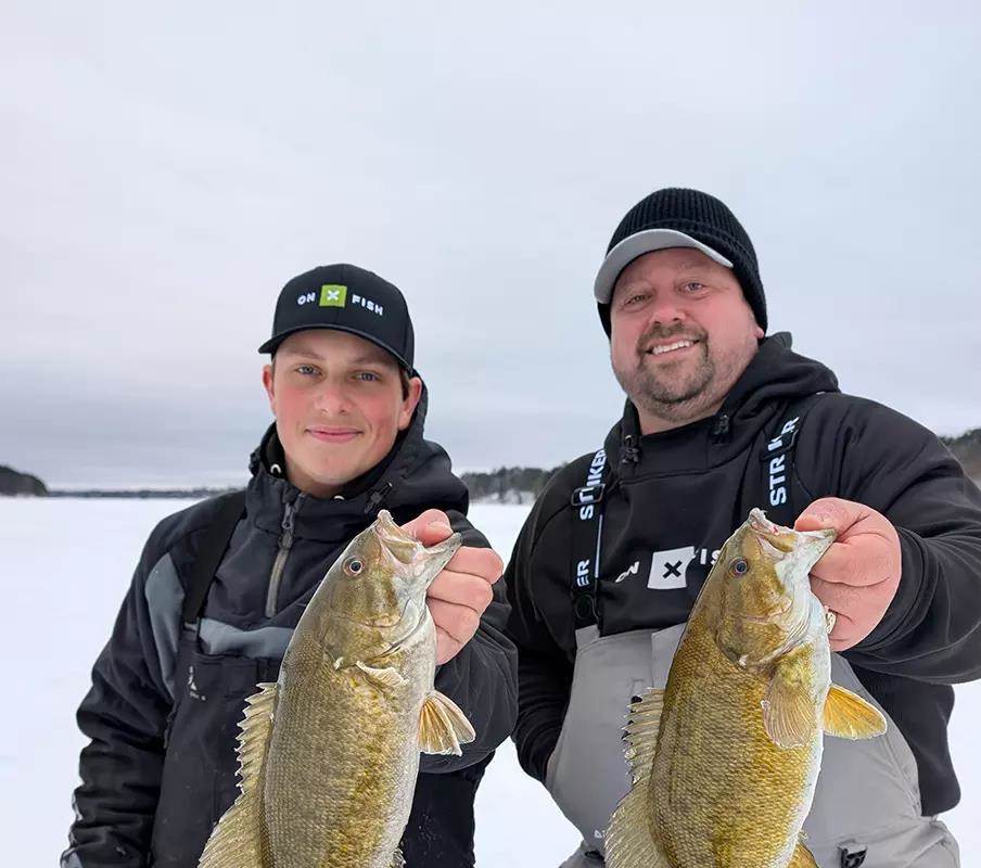 Two anglers hold two smallmouth bass caught through the ice. 