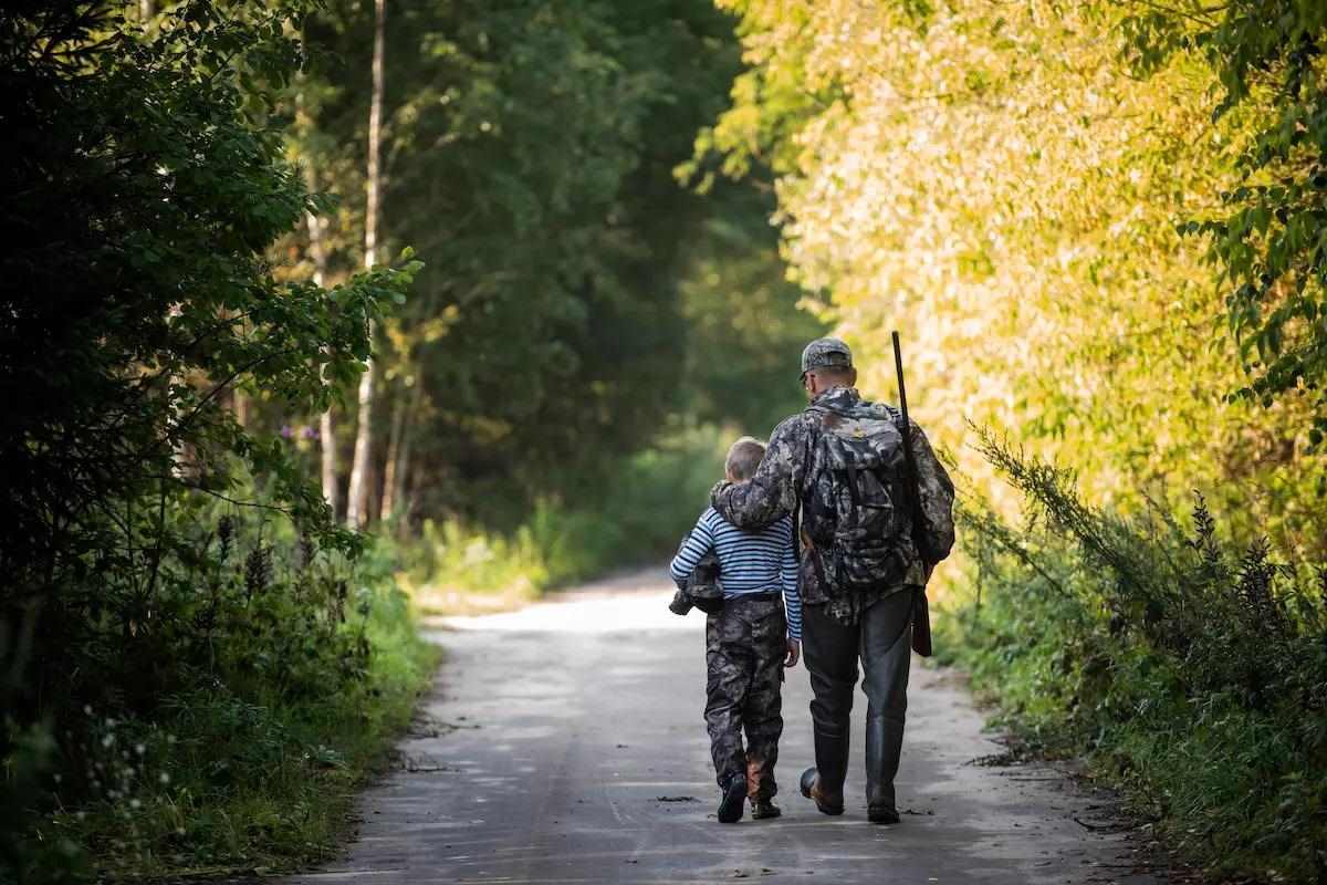 A father and son walk a wooded path on the way to go hunting.