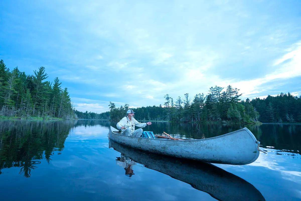 A fly angler in a canoe on a lake at low light. 