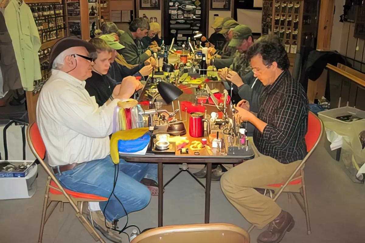 Several men sitting at a table tying flies. 