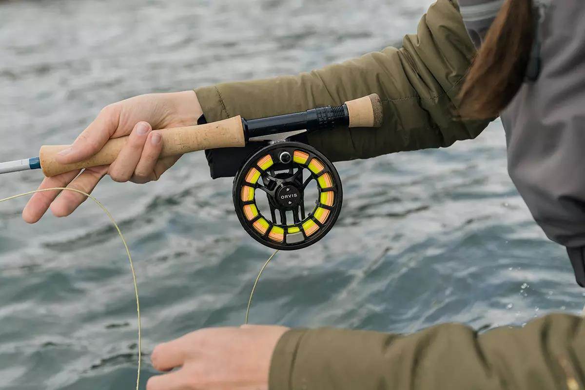 A fly angler's arm holding a fly rod and reel on a river. 