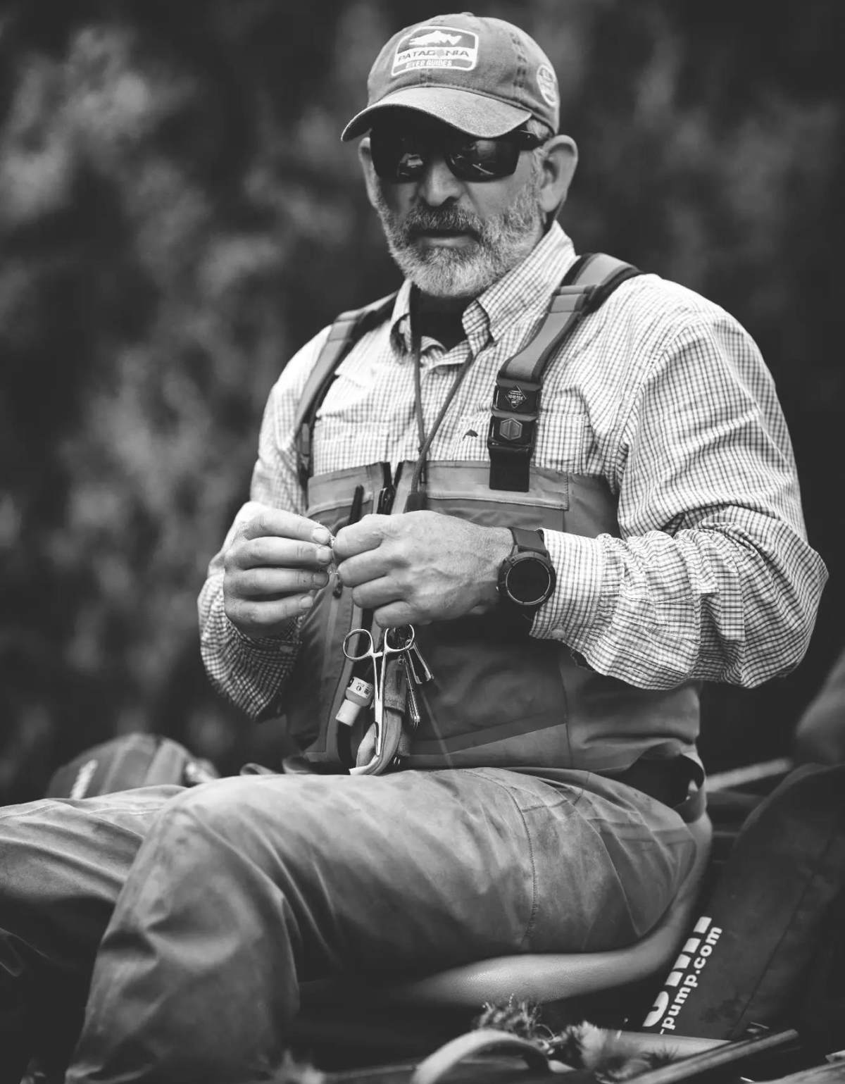 A grayscale image of a fly-fishing guide gazing onto the water from a seat on a raft.