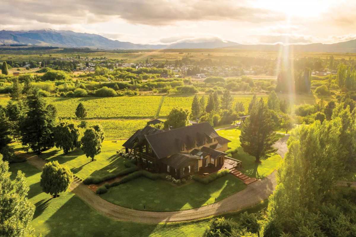 A drone photo of a large house or lodge in a green valley and bright sun.