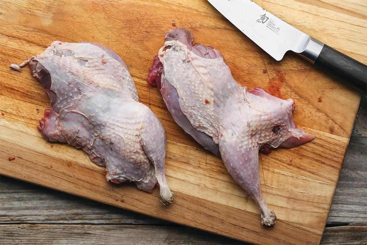Two sharp-tailed grouse halves plucked on a cutting board.