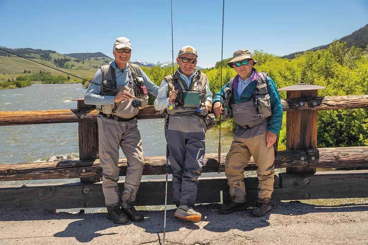Three fly anglers standing on a bridge over a river.
