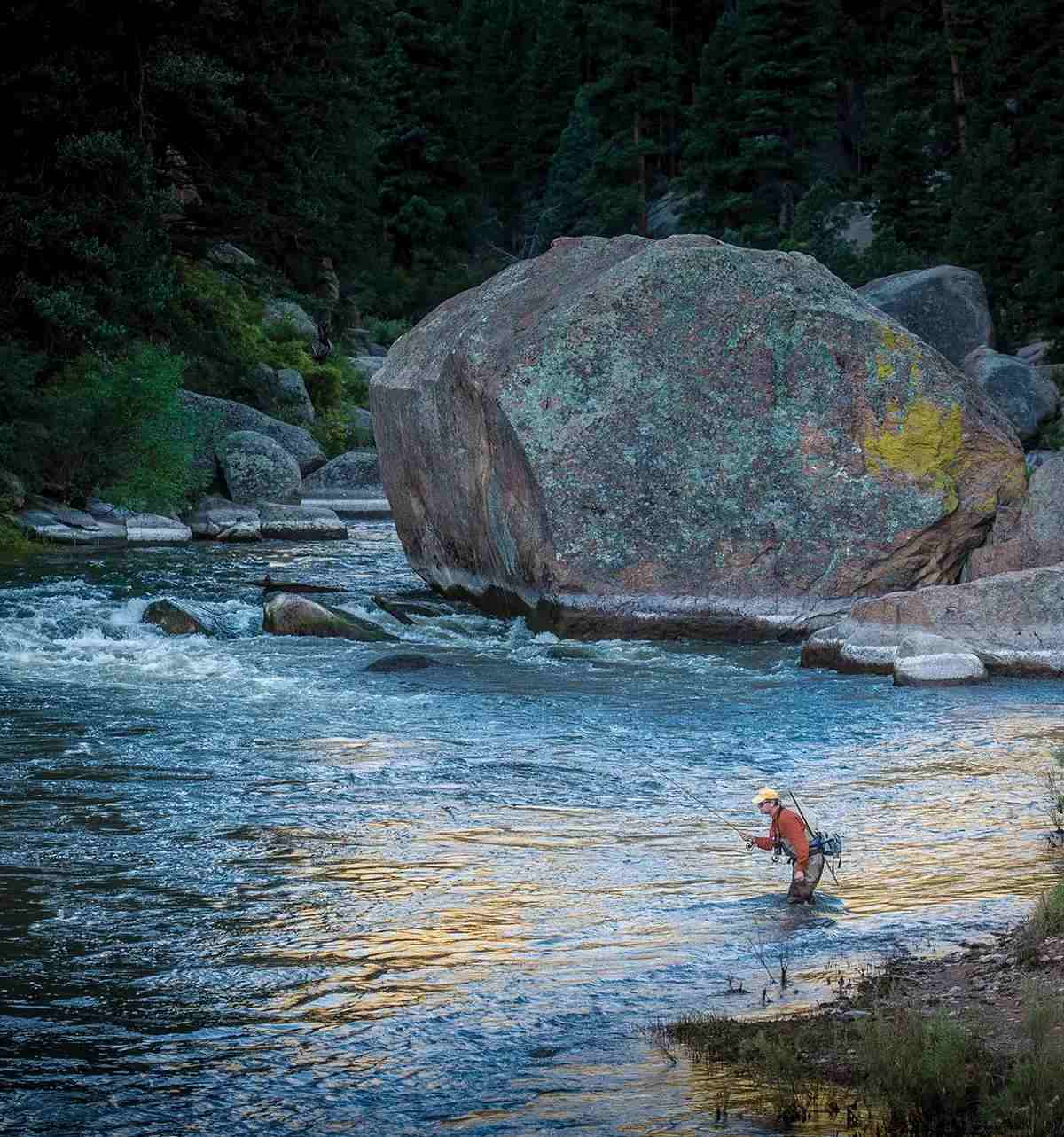 A fly angler drifting a run on a boulder-strewn river. 