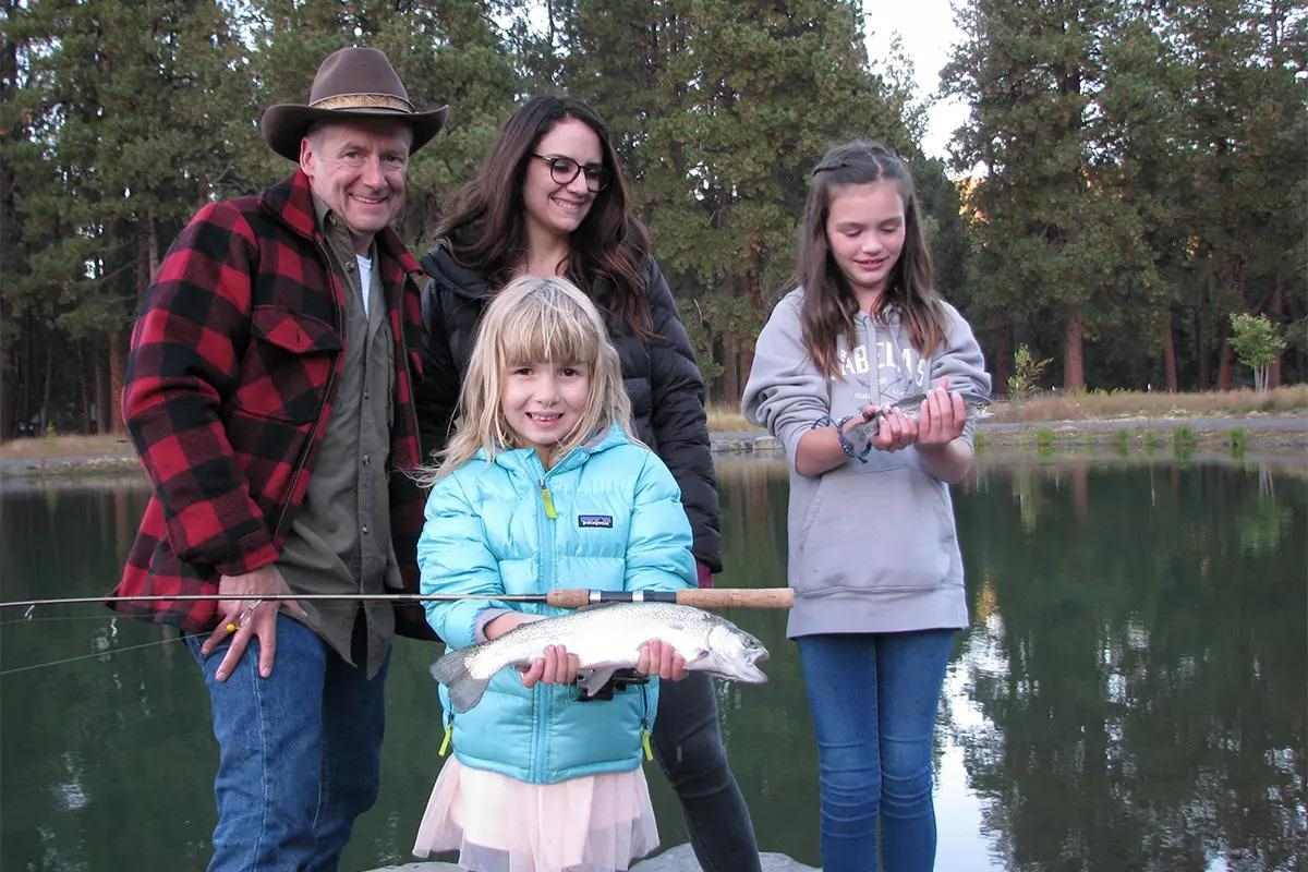 A family fishing holds two caught trout at a lake. 
