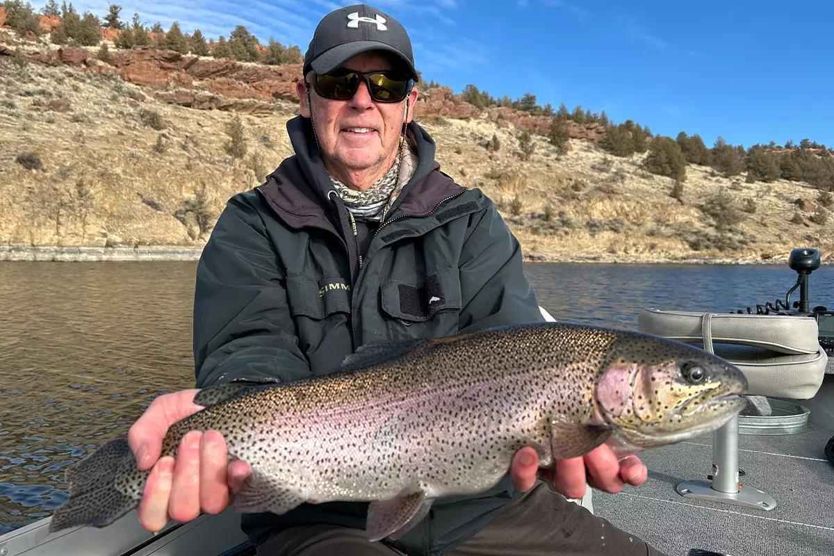 An angler holds up a large rainbow trout caught from his boat.
