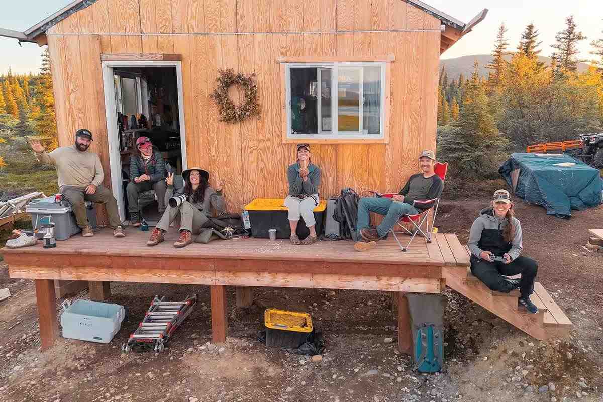 Six people smiling for the camera sitting on the porch of a newly built cabin.