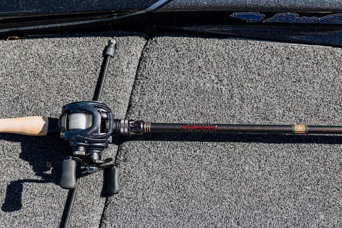 A baitcasting rod and reel lie on a bass boat deck.
