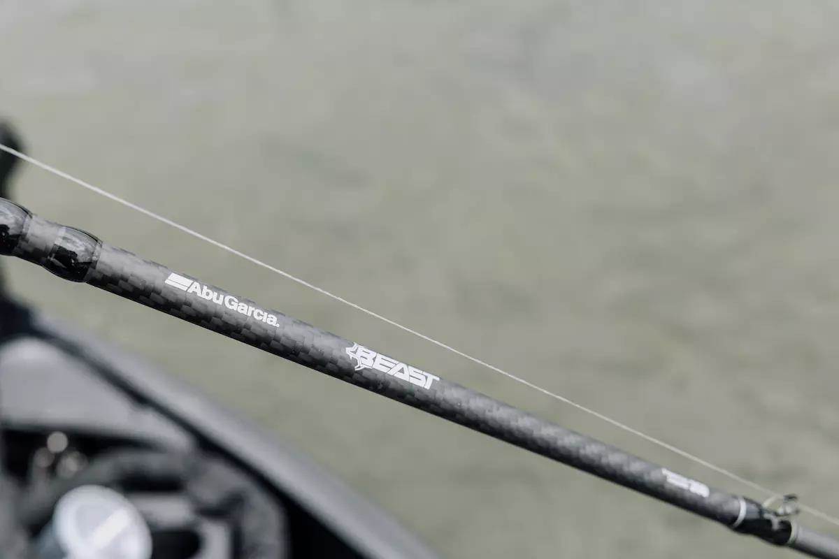 An angler holds a fishing rod with water in the background. 