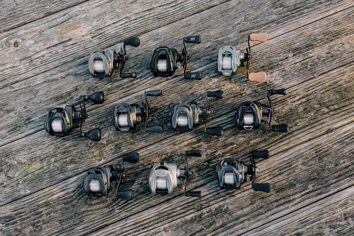 Ten baitcasting reels lie on a wooden deck.
