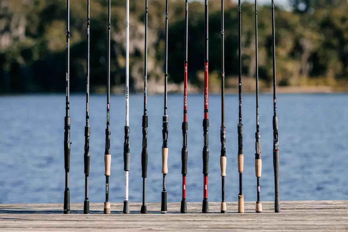 A group of blank baitcasting rods stood up on a wooden dock with a lake in the background. 