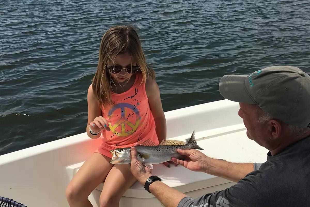 Man shows spotted seatrout to girl who caught it