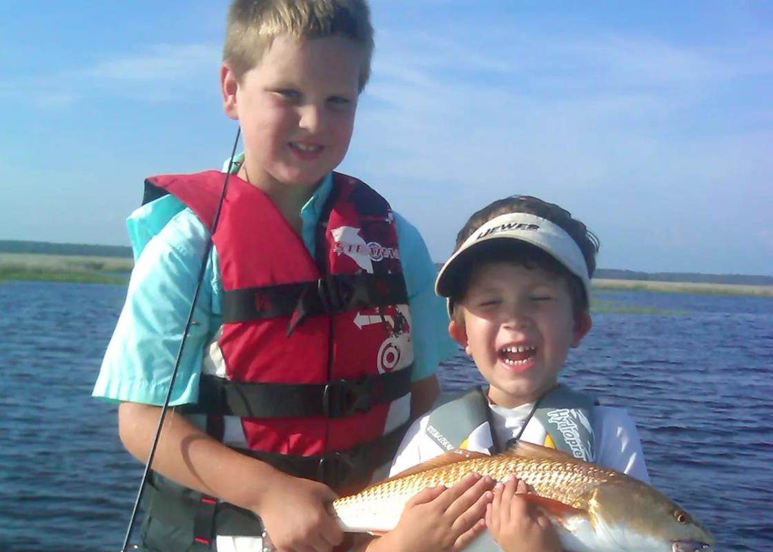 two boys in life jackets holding a red drum
