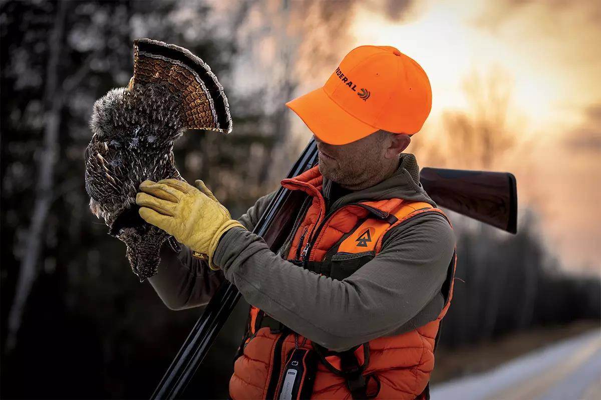 A hunter with orange keeps a tank to show the fan and the colors of the tail on the back.