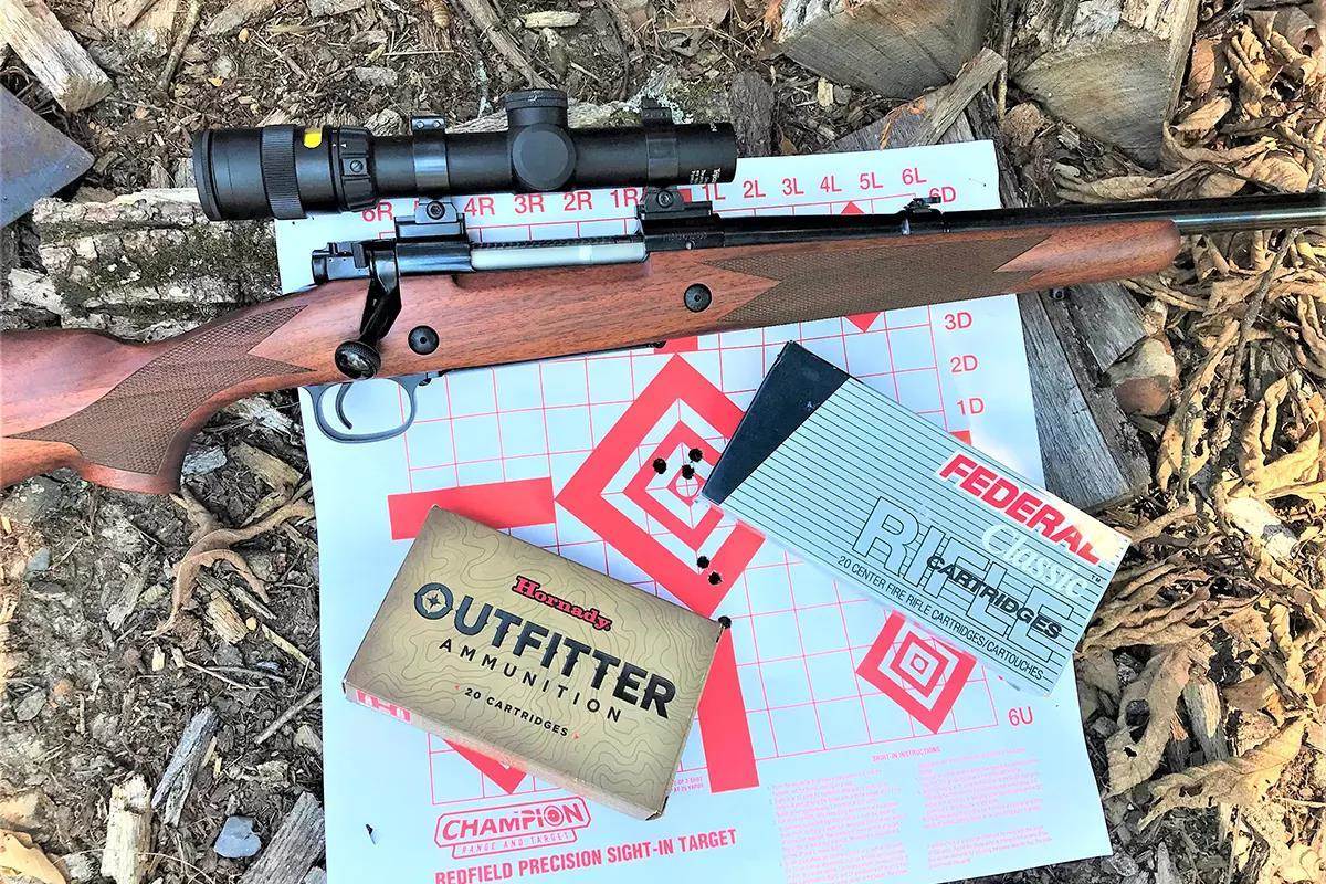 A hunting rifle and ammo boxes lie on top of a shot target in the leaves. 