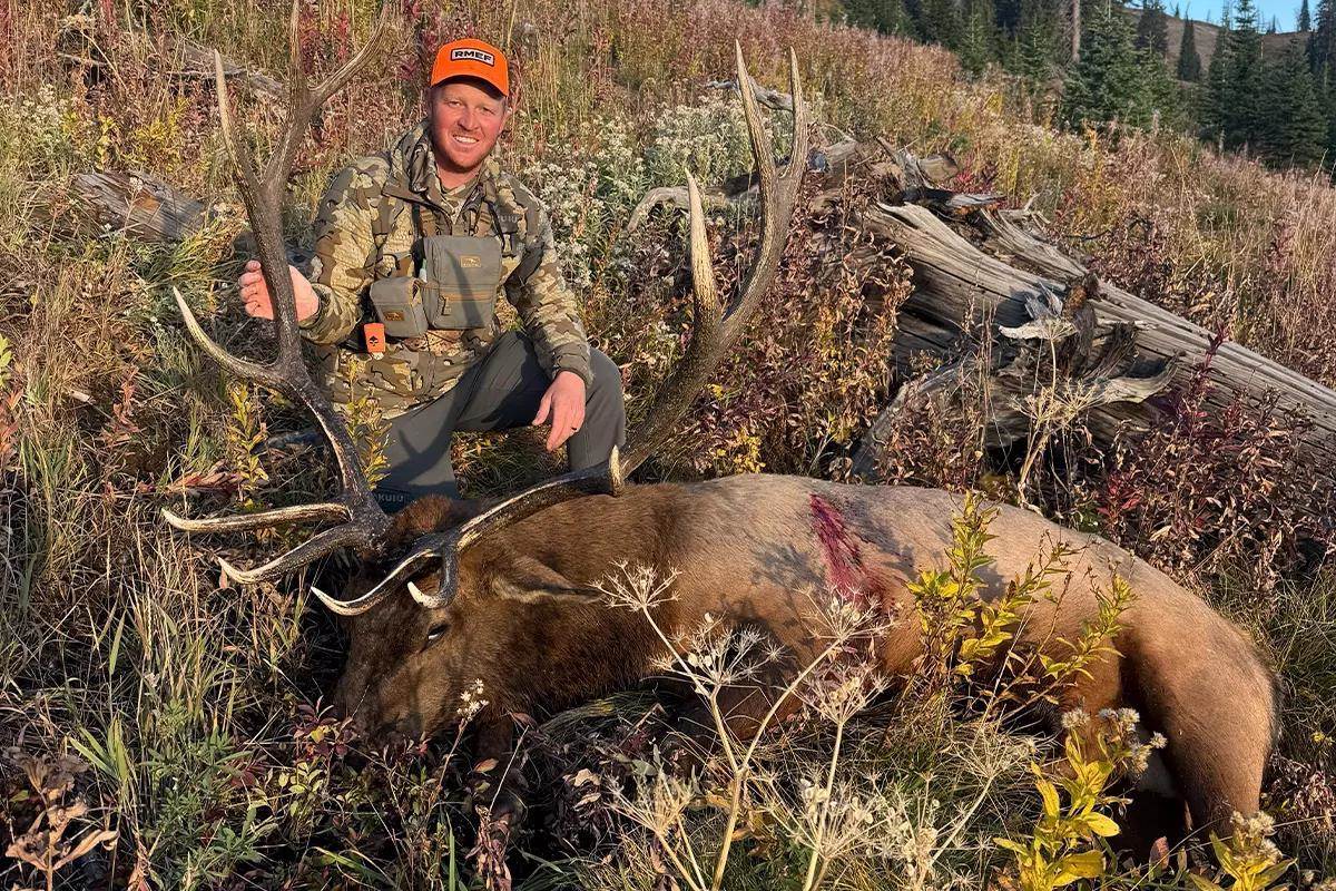A hunter poses with a downed bull elk on the side of a mountain in Wyoming. 