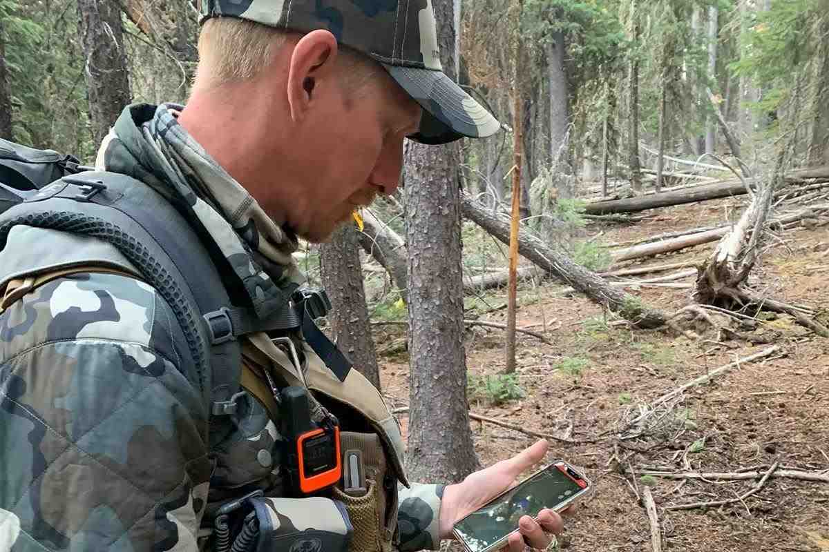 A hunter in the woods checks a phone to find his location on a map.