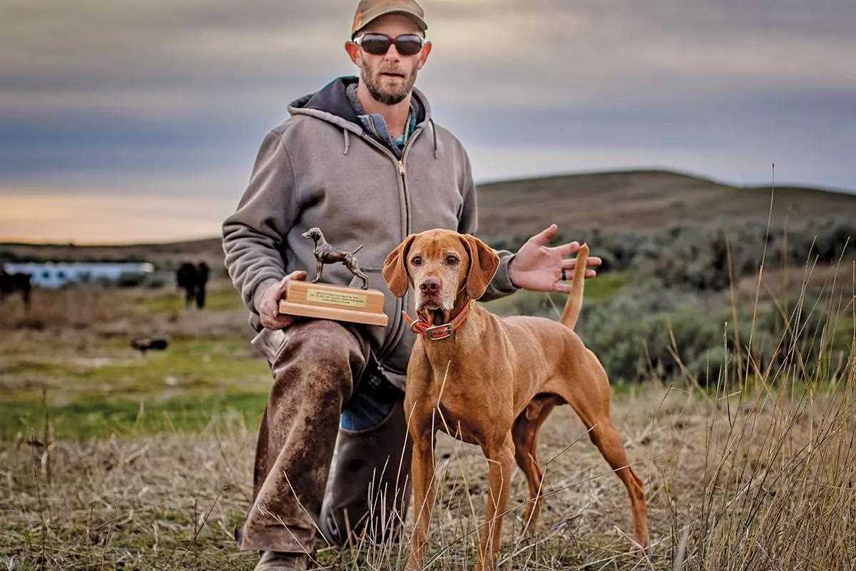 A viszla and its handler stand for a winners photo with a trophy.