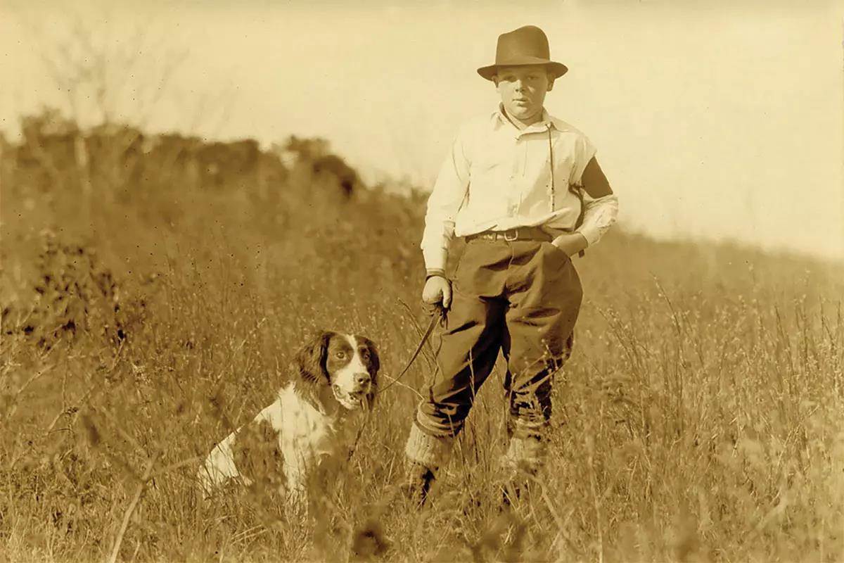 A young boy stands in a field with his dog on a leash.