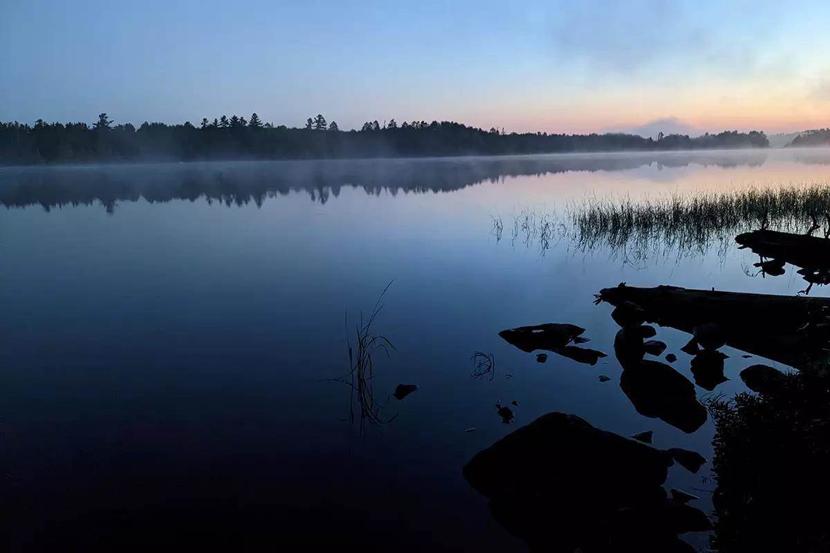 A serene early-morning scene from the Boundary Waters; fog on the water. 
