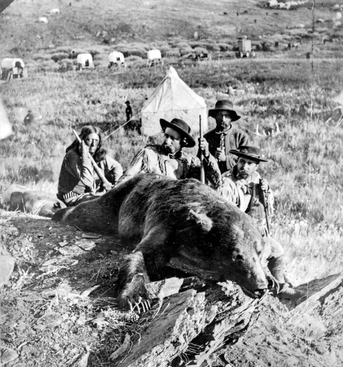 Black and white photo of General Custer sitting with a few others behind a large grizzly bear they shot. 