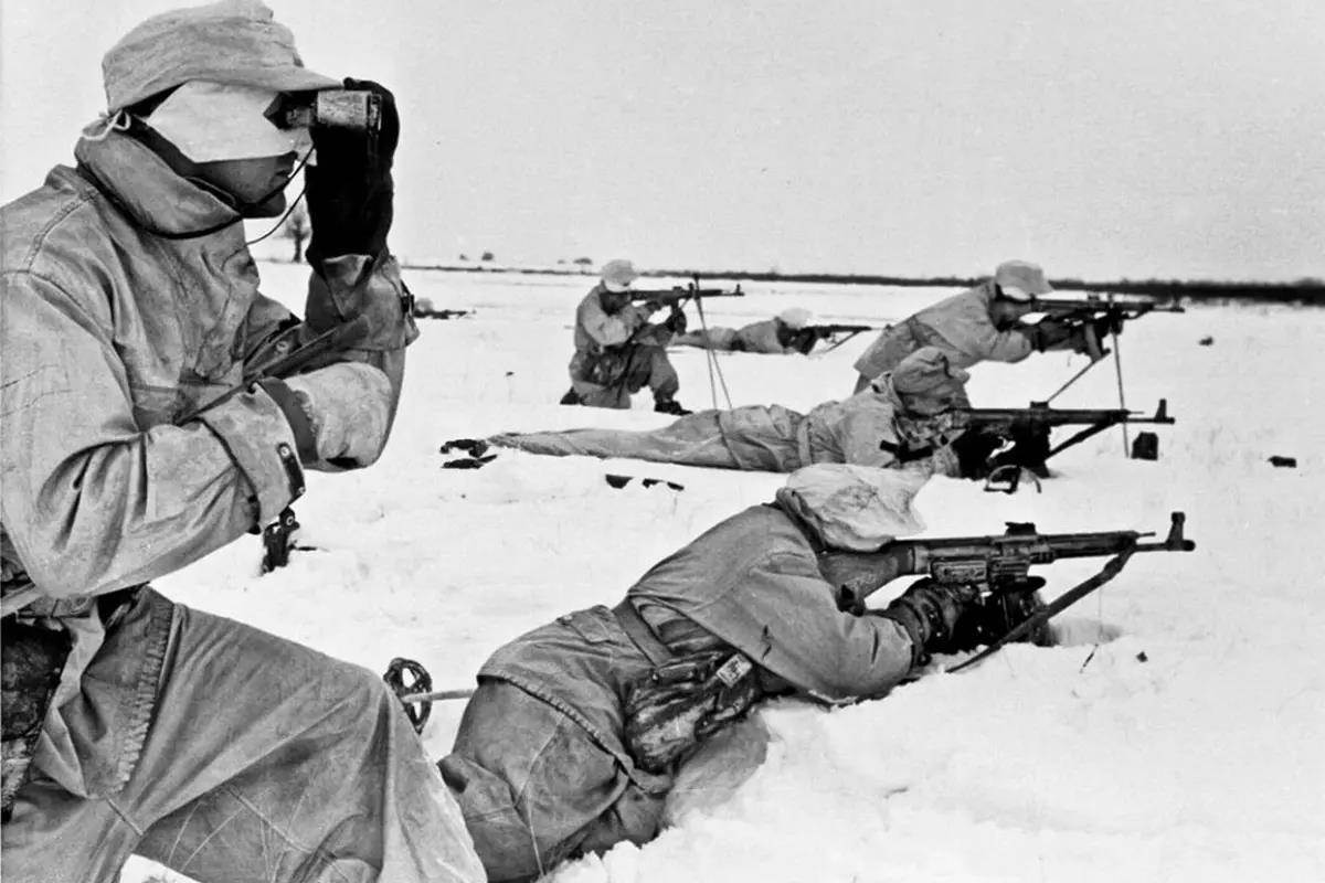Six German soldiers in white uniforms aim their rifles in the snow during World War II