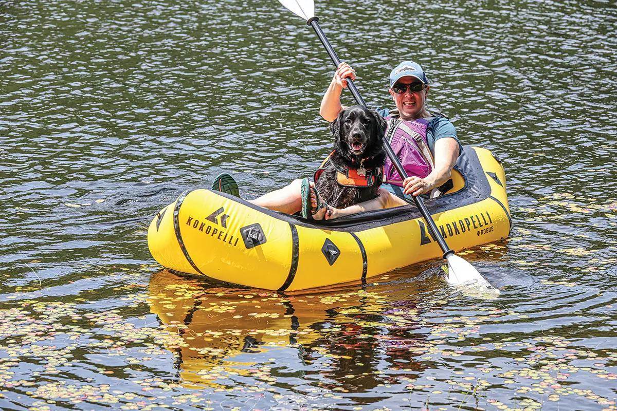 A paddler and their dog in a small yellow raft on the water. 