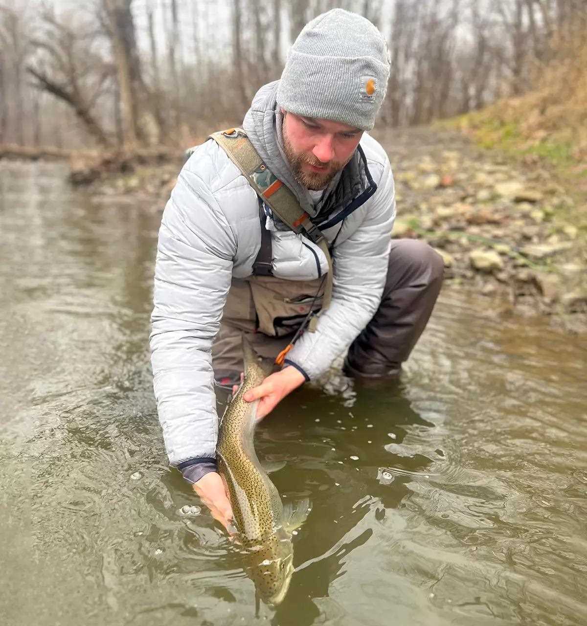 A fly angler holding a rainbow trout in the water on a river.