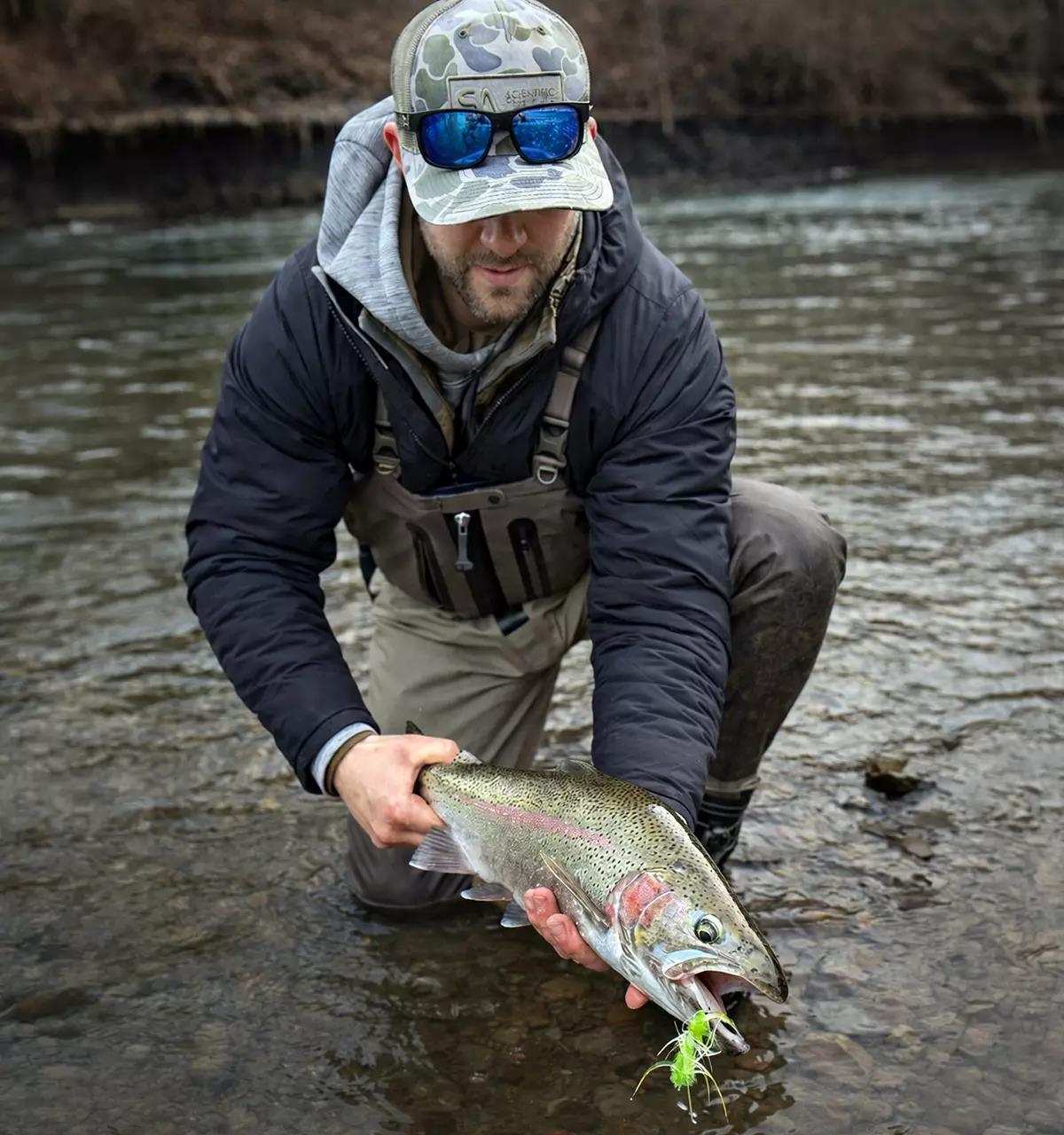 A fly angler holding a large rainbow trout just above the water's surface on a river.