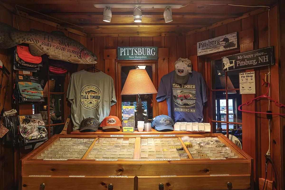 The interior of a fly shop with shirts, hats, and fly bins. 