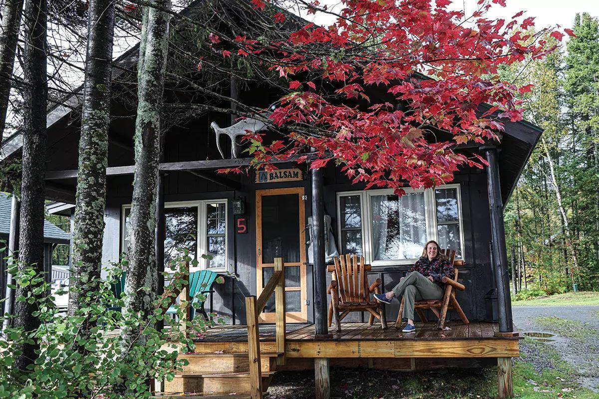 A cabin at a fishing resort; a woman sitting on the deck in an Adirondack chair. 