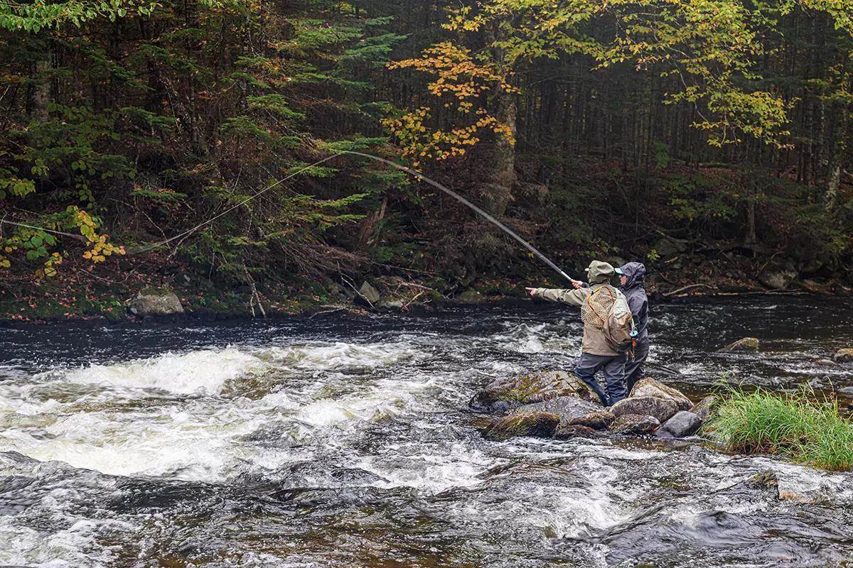 Two fly anglers on a swift river; one is casting the other is pointing. 
