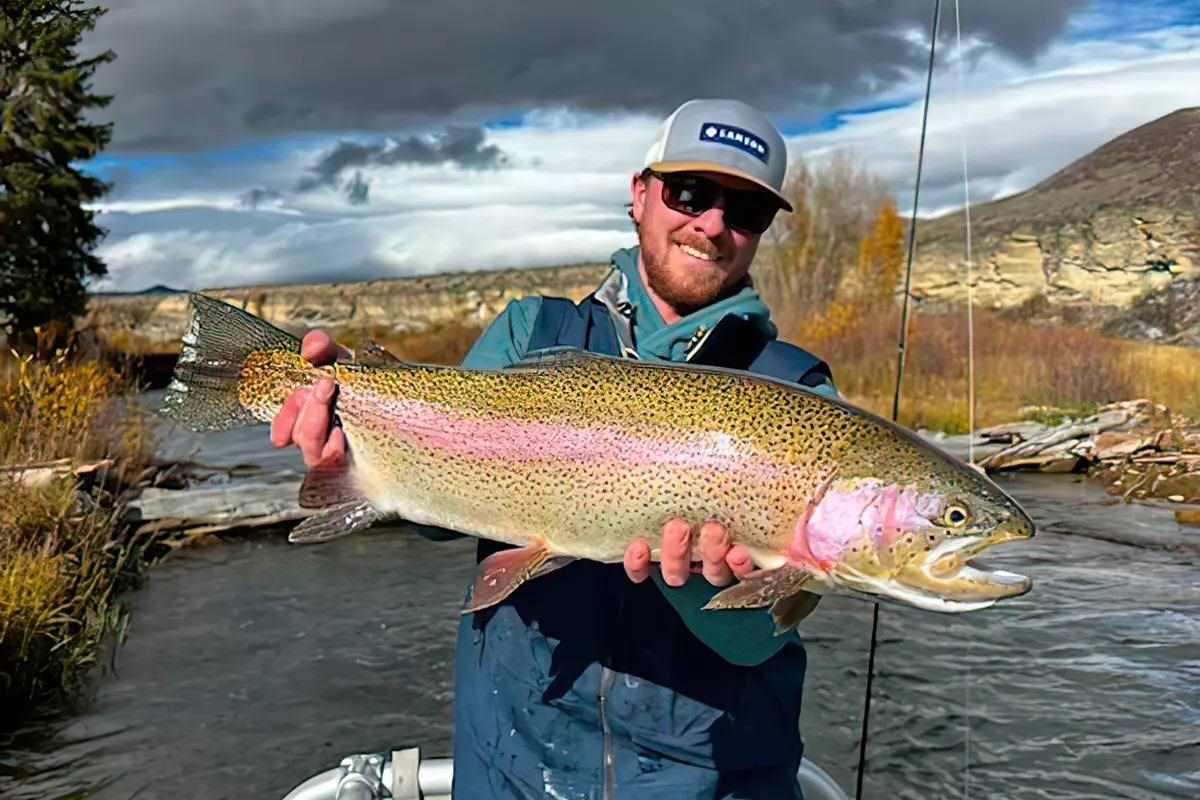 A fly angler holding a large rainbow trout. 