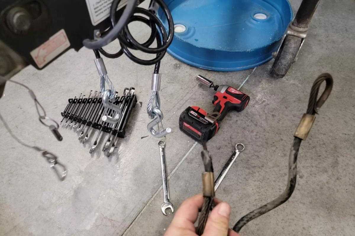Some wrenches, a power drill, and a hitch wheel on a concrete floor.