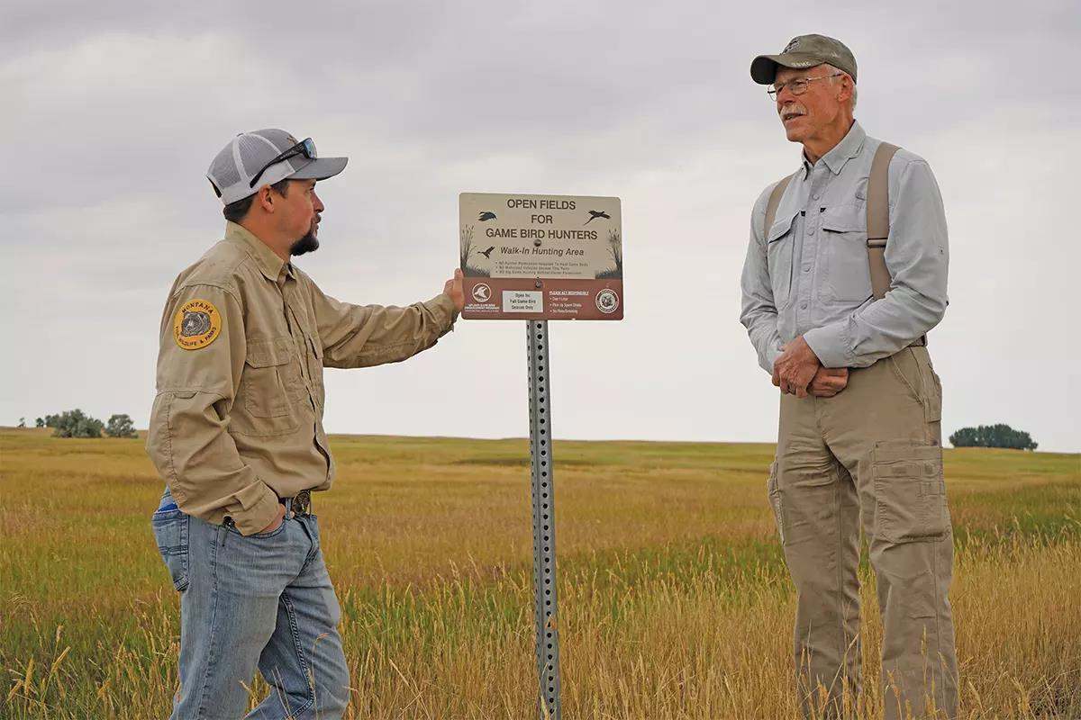 Two and managers stand near a sign as they talk about the prairie habitat.