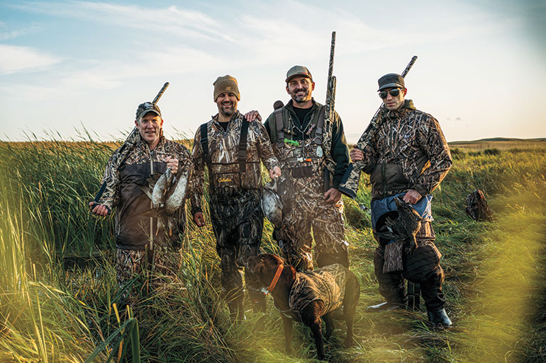 four waterfowl hunters with ducks and chocolate lab
